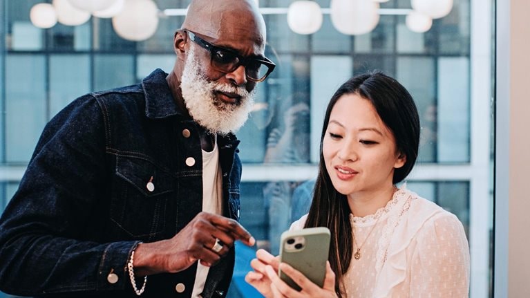 A woman shows a coworker something on her smart phone in an office setting.