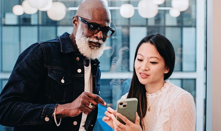 A woman shows a coworker something on her smart phone in an office setting.