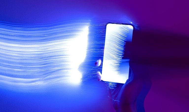 Close-up photo of a hand holding a mobile phone with light streaks trailing out of it.