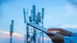 Close up of a hand touching a digital tablet near a 5G communications tower