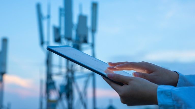 Close up of a hand touching a digital tablet near a 5G communications tower