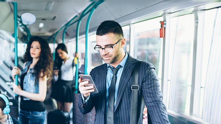 Front view of a businessman looking at his 5G phone while riding on public transportation.