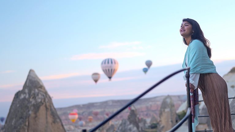 Portrait of young female tourist watching hot air balloons from a balcony on a cliff