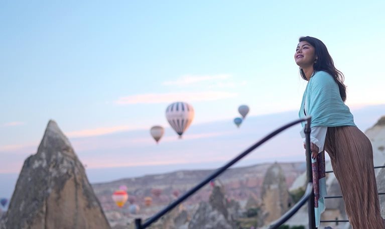 Portrait of young female tourist watching hot air balloons from a balcony on a cliff