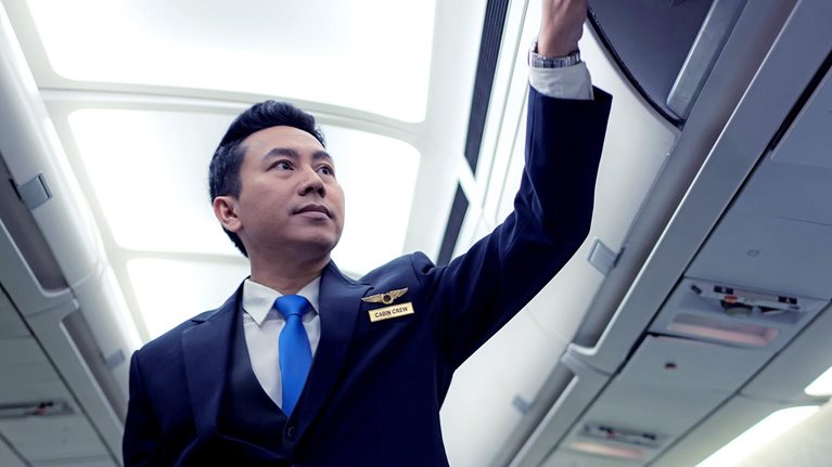 Image of a flight attendant closing overhead bins on an empty plane.