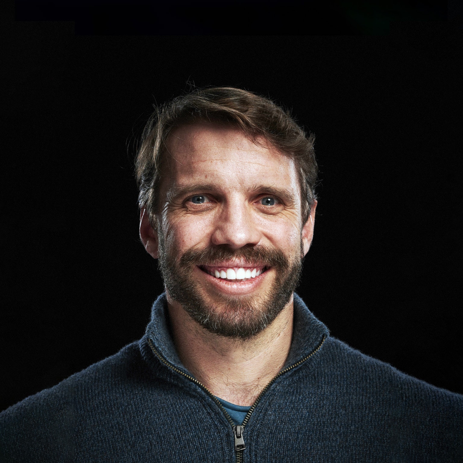 Ryan Petersen wearing a navy blue half-zip-collared sweater against a black studio backdrop.