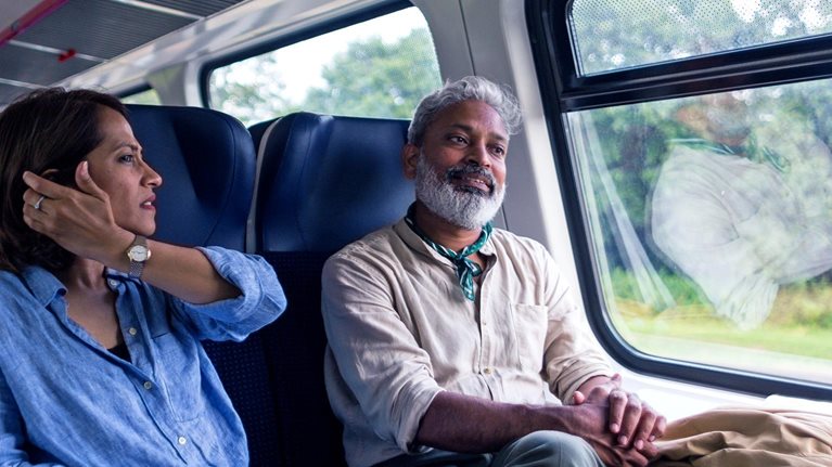 A mature Indian tourist couple riding in a commuter train in Lithuania, talking, having fun, and looking out the window.