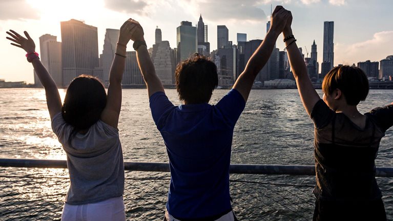Three friends holding hands in celebration across the water from a city skyline