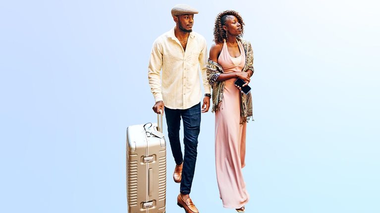 Wide shot of couple arriving in hotel courtyard with rolling luggage while on vacation