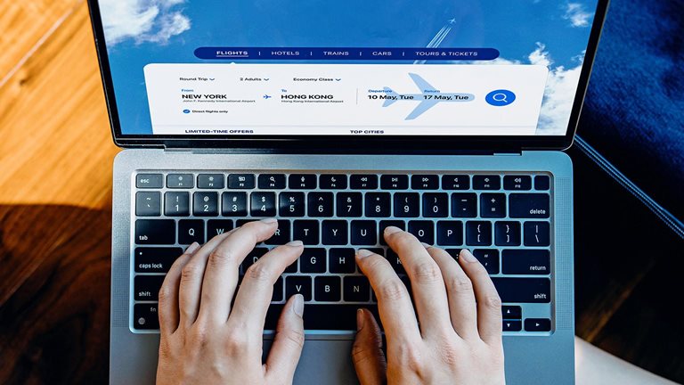 High angle shot of young woman booking flight tickets on airline website with her laptop, a packed suitcase by her side. 