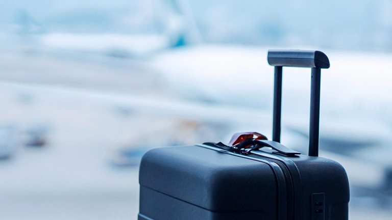 A black suitcase in front of the window at international airport terminal, with blurred airplane in the background.