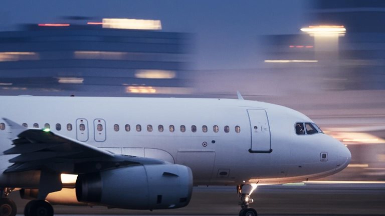 Image of an airplane taking off at night with blurred lit buildings in the background.