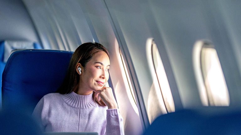 A woman passenger working mid-flight stops to gaze out her airplane window.
