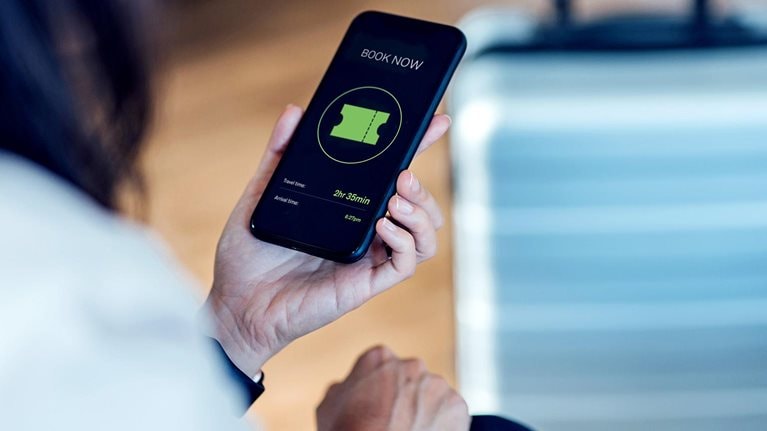 Image of a person purchasing a ticket on a mobile device with a suitcase in the background.