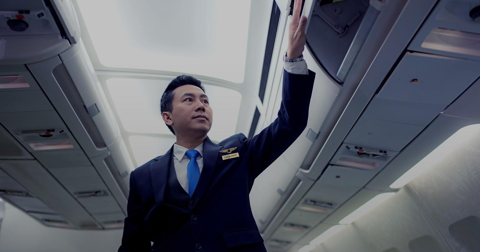Airline crew member standing inspecting the overhead bin inside of the airplane