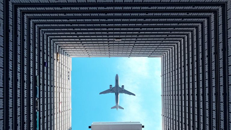  Airplane flying overhead, viewed through the open center of a high-rise building courtyard.
