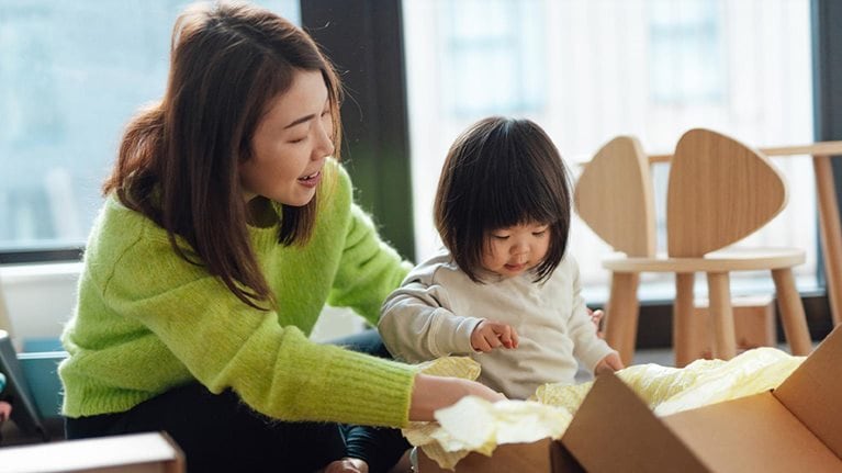 Young Asian mother unpacking parcel from online shopping with her toddler