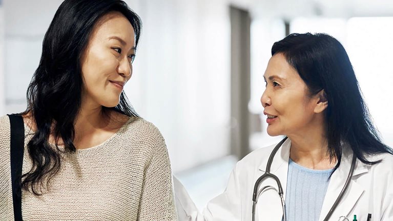 woman doctor comforting woman patient walking down hospital hallway