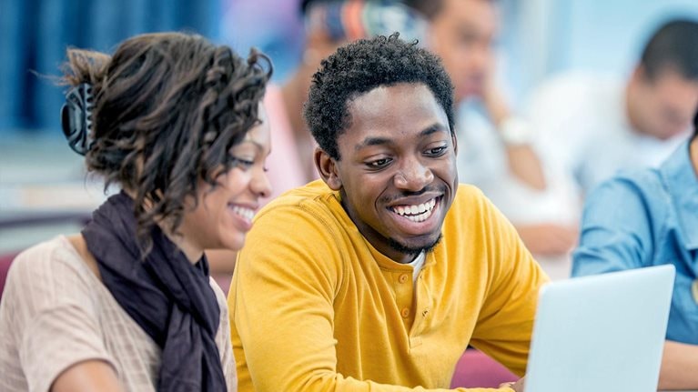A multi-ethnic group of college age students surfing the web and researching a paper together. - stock photo