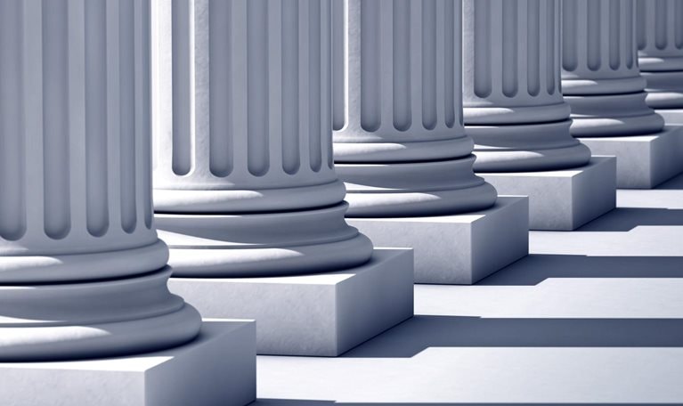 A deep row of stone columns with long linier shadows.