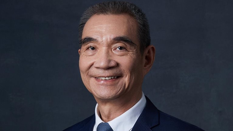 Portrait of smiling Justin Yifu Lin against a dark blue textured background. 