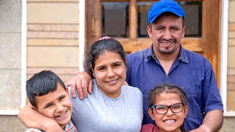 Portrait of a rural Latin American family in front of their new house and looking at the camera smiling