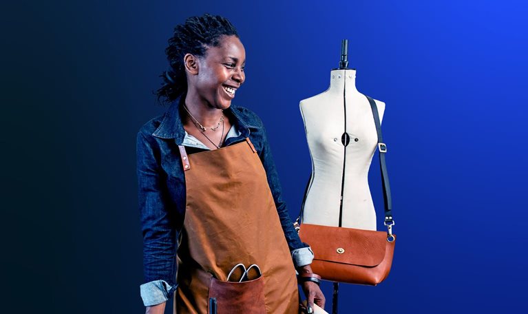 An image of a small business owner sharing a laugh at her design studio, where she makes leather goods to sell in her shop.