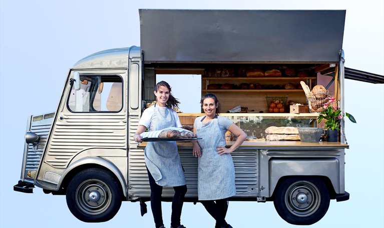 Image of confident women standing next to their vintage van that has been converted into a foot truck.