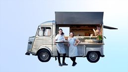 Image of confident women standing next to their vintage van that has been converted into a foot truck.