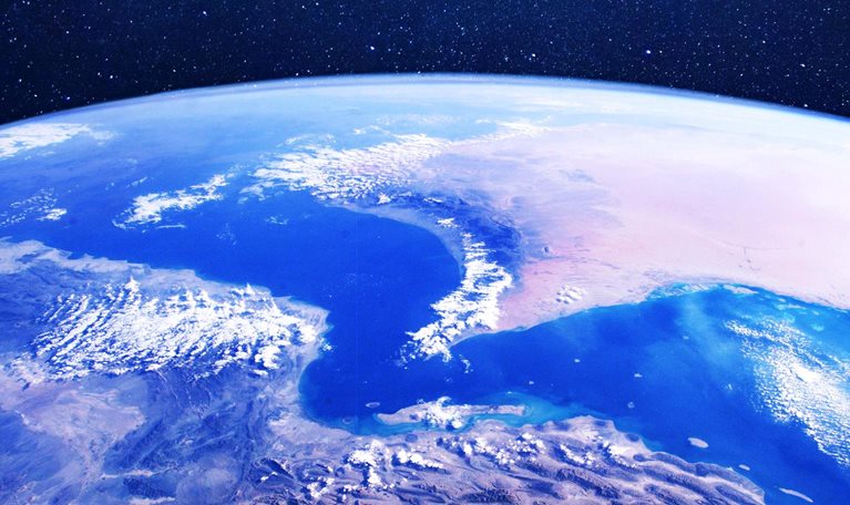 A view of Earth from space centered on the Strait of Hormuz. The curve of the planet, deep blue seas, desert landmasses, and scattered clouds are visible.