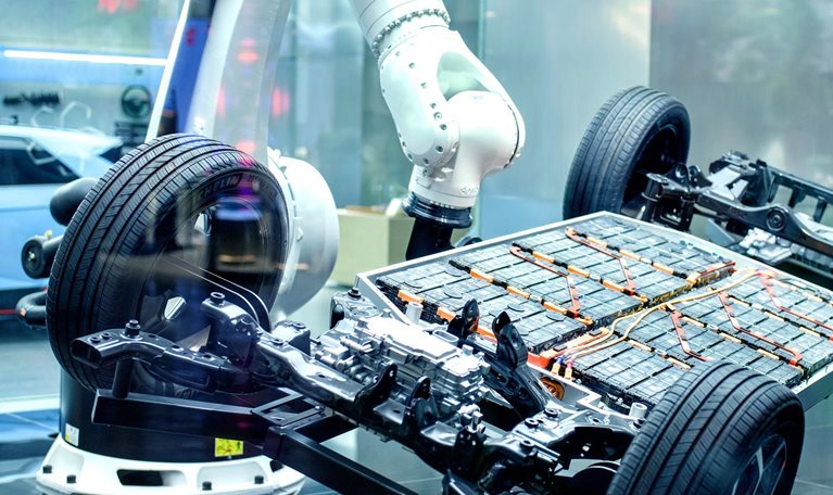 The exposed chassis and battery platform of an electric vehicle surrounded by robotic arms in a high-tech manufacturing or display environment.