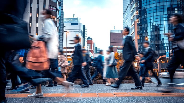 Motion-blurred businesspeople in Tokyo walking across an intersection on their way from work. 