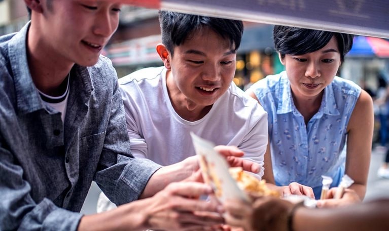 Three people ordering food at a street food counter