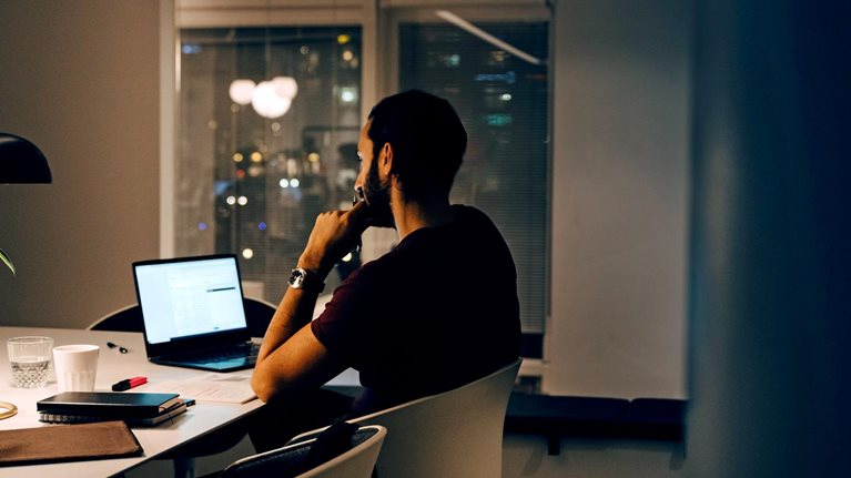 Side view of dedicated male professional working late at illuminated desk in coworking space