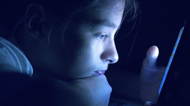 Child staring at phone in a dark room