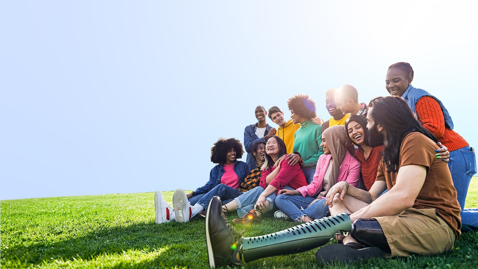 Diverse multiethnic people enjoying themselves outdoors sitting on the grass in a city park
