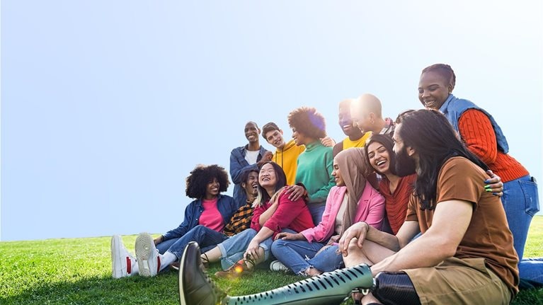 Diverse multiethnic people enjoying themselves outdoors sitting on the grass in a city park
