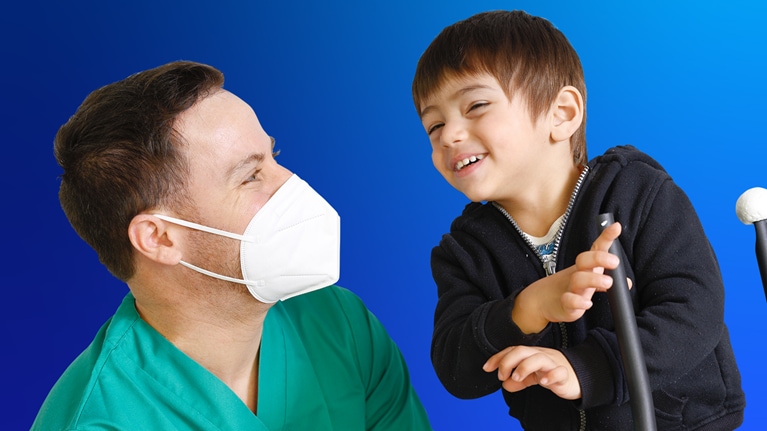 A healthcare professional in mask looking affectionately at a child who is gesturing with his hands.