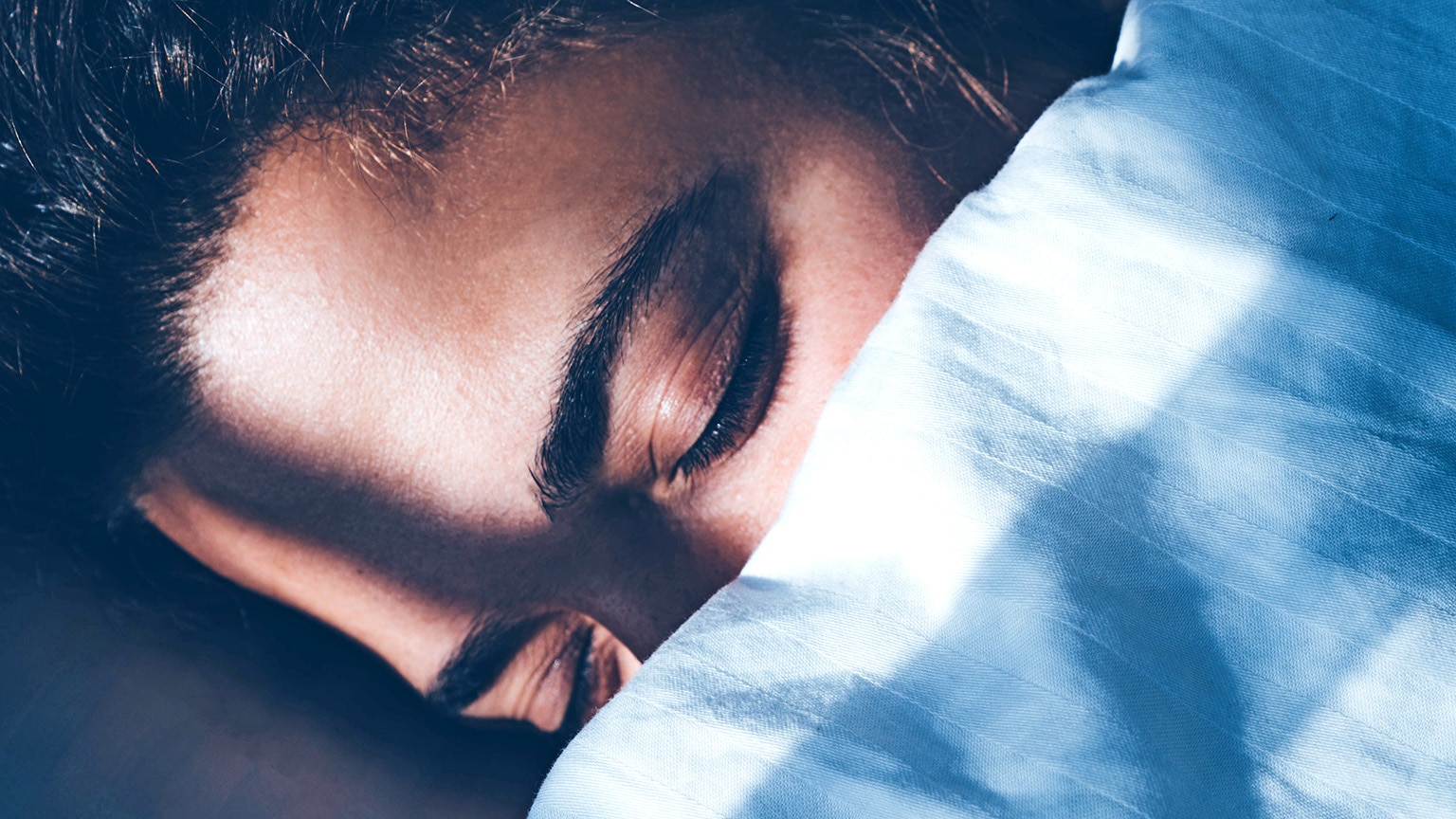 Close-up of a person sleeping with the covers over the bottom half of their face.