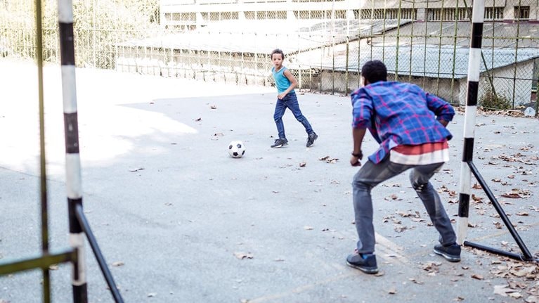 Image of a father and son playing soccer on an urban blacktop court.