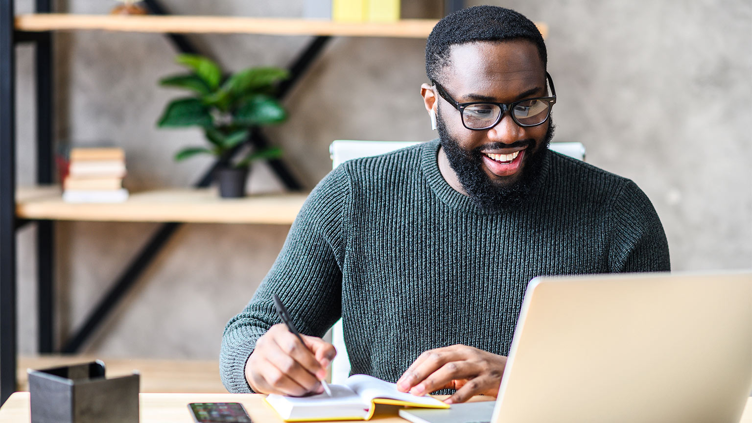 A man working on a laptop and writing notes in a book