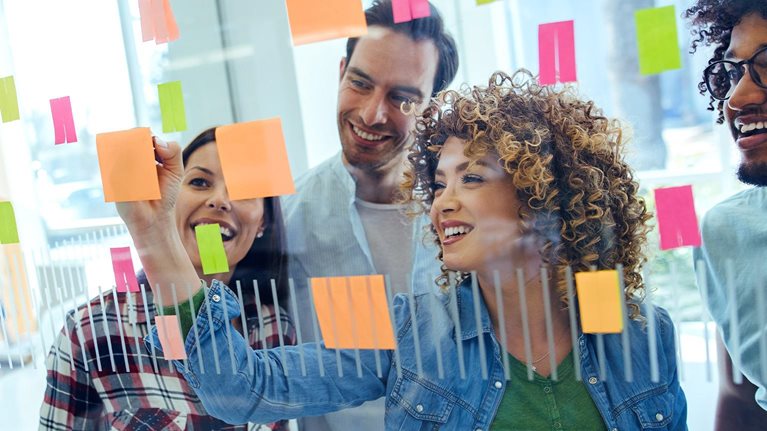 Image of a diverse team in an office brainstorming in front of a glass wall.