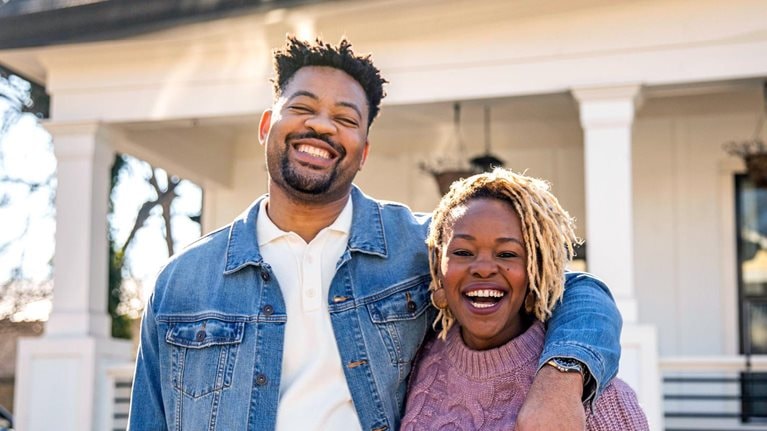 Portrait of husband and wife embracing in front of home