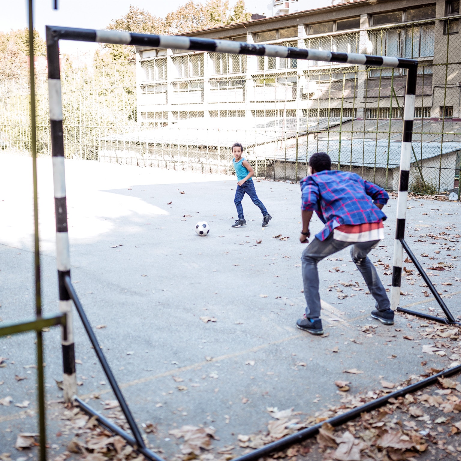 Image of a father and son playing soccer on an urban blacktop court.
