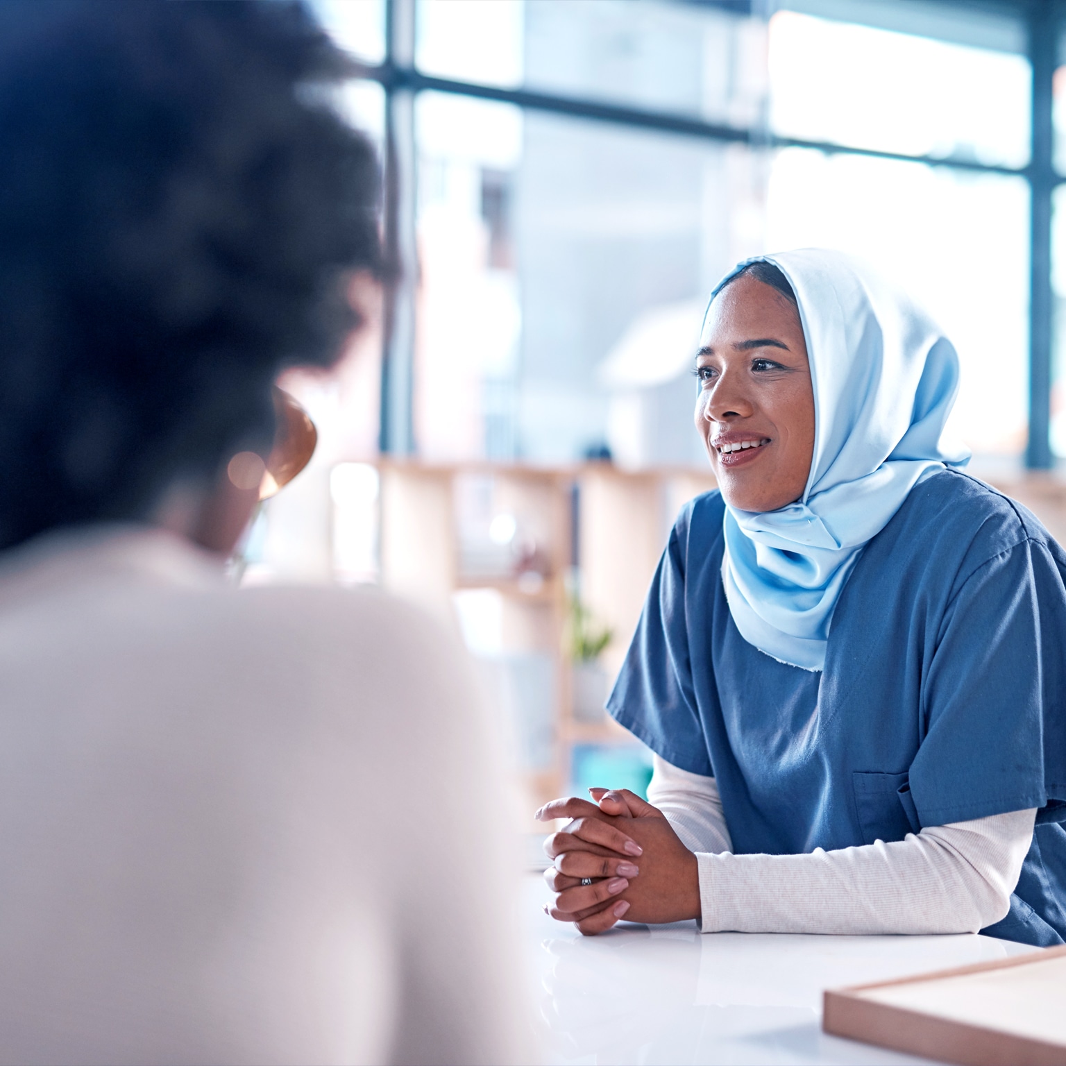 A discussion in progress between three participants, with a woman with her head and hands covered facing the viewer