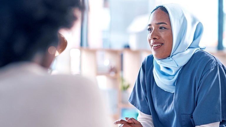 A discussion in progress between three participants, with a woman with her head and hands covered facing the viewer