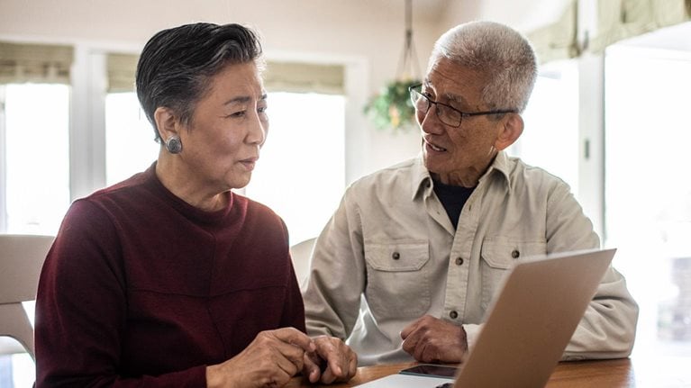 elderly couple talking in front of open laptop