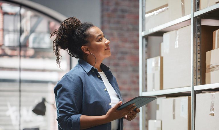 Portrait of a Manager Checking Inventory, Writing in Tablet Computer. Black Woman Working in a Warehouse Storeroom with Rows of Shelves Full of Parcels, Packages with Orders Ready for Shipment. - stock photo