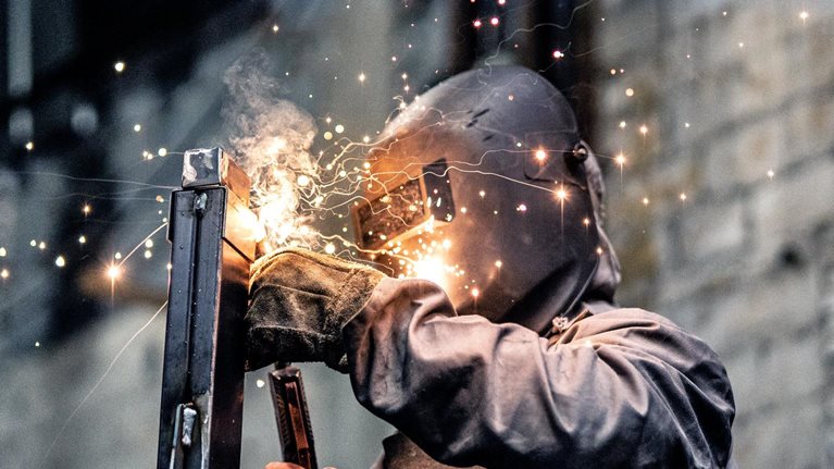An individual clad in protective welding attire, working on a steel component while sparks scatter.