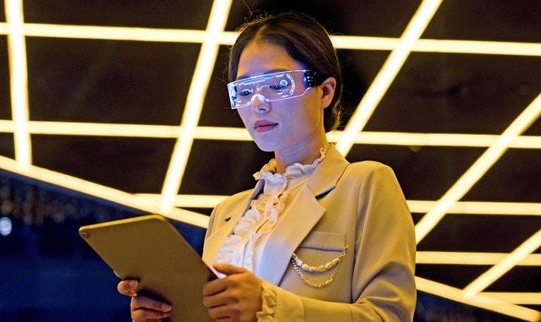 Image of a person wearing tech glasses and a lab coat looking at a tablet.